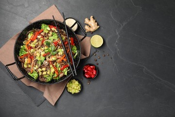 Wok with noodles, mushrooms, vegetables and other products on black table, flat lay. Space for text