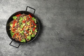 Stir fried noodles with mushrooms and vegetables in wok on grey table, top view. Space for text