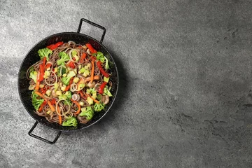 Gordijnen Stir fried noodles with mushrooms and vegetables in wok on grey table, top view. Space for text © New Africa
