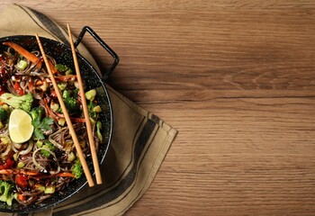 Stir-fry. Tasty noodles with meat in wok and chopsticks on wooden table, top view. Space for text