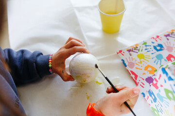upper view of child hands coloring the egg with brush on the table