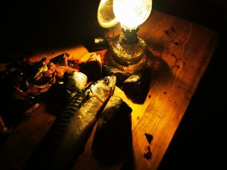 Kerosene lamp with flame light. Vintage photo with old kerosene lamp and mackerel fish