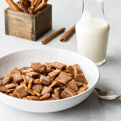 A bowl of cinnamon toast crispy cereal with milk and cinnamon sticks in behind.