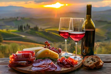 Foto op Canvas  Red wine and Italian prosciutto with cheese on the wooden table against a landscape background in Tuscany, Italy at sunset.  © Maru_sua