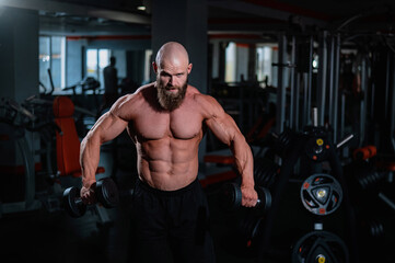 A muscular shirtless man lifts dumbbells to the sides with dumbbells in the gym.