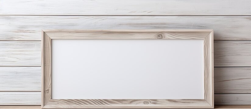 A beige rectangular picture frame made of natural hardwood sits on a wooden table in a room with a white wooden wall and molding on the ceiling