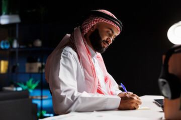 At his desk, a businessman from the Arab world skillfully browses the internet while focused on his...