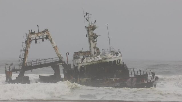 Shipwreck Zeila in the crashing waves at sea from beach near Swakopmund on Namibia Skeleton Coast, Africa under grey solemn sky.