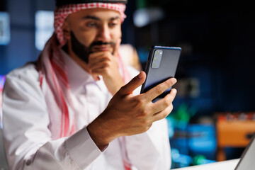 A healthy Arab businessman using a mobile phone at his desk. Detailed image of a Muslim guy surfing...