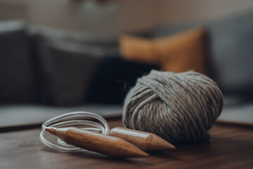 Ball of grey chunky wool yarn and large circular knitting needles on a wooden table.