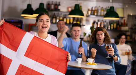 Screaming young adult sports fans rooting for favorite team and waving flag of Denmark while...
