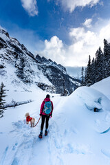 Backpacker Girl with her dog admires beautiful views of snow covered mountains near Lake Louise