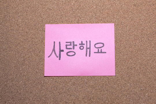 A pink sticky note with a "I love you" message in Korean on a cork board. Formal communication. Love. Concept of human relationships.