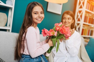 Cute little girl presenting a bouquet of pink tulips to her mother at home. Mother`s day concept