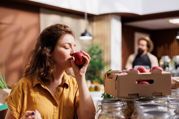 Woman enjoying the smell of organic farm grown apples in eco friendly zero waste store. Client...