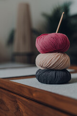 Stack of three balls of DK yarn with a wooden crochet hook on a table, shallow focus.