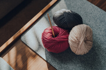 Three balls of DK yarn and a crochet hook on a wooden table, sunlight from the window, shallow...