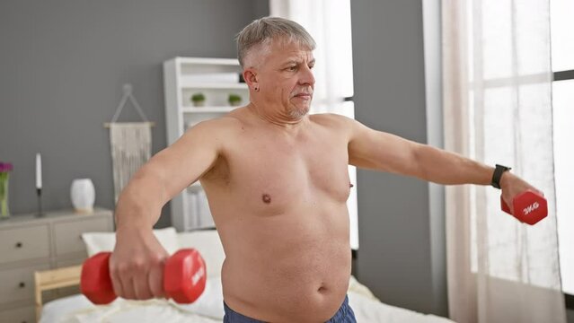 A senior man works out with dumbbells in a modern bedroom, maintaining fitness and health at home.