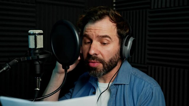 Male voice actor talking to a microphone a recording some lines in a soundproof studio, seen up close