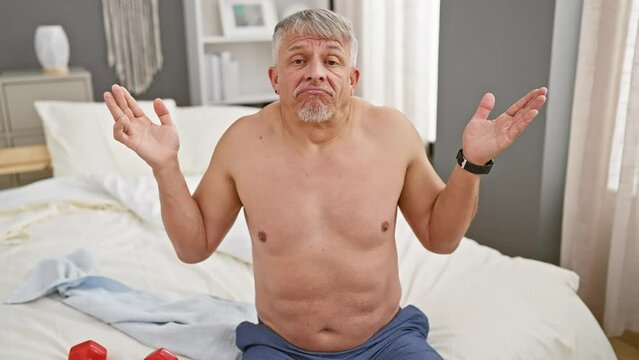 Grey-haired middle age man, shirtless and clearly mad, screaming loud in the bedroom. facing sideways with hand cupping his mouth for amplifying his shout of frustration.