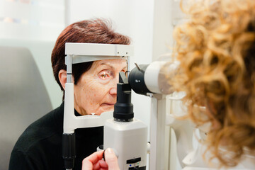 Elderly woman checking her vision using biomicroscopy machine in a clinic - Powered by Adobe