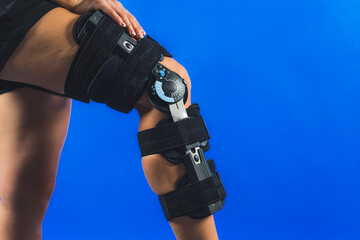 closeup shot of a girl putting her hand on a protective band on her knee injury, trauma and rehabilitation concept, blue background. High quality photo