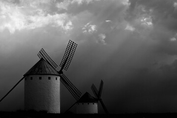 Two silhouetted windmills standing stark against a backdrop of textured clouds, captured in a striking monochrome tone