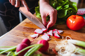 A close up of girl's or woman's hands peeling and cutting vegetables with knife making salad	
