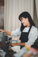 A smiling barista in a black apron arranges cups at a coffee shop, her pleasant demeanor adding warmth to the ambiance.