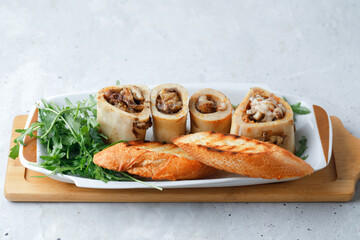 Homemade Roasted Beef Bone Marrow with bread crumbs, greens rocket arugula salad and croutons on plate, wooden board grey background. Top View.