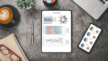 Office desk workplace with business chart on screen tablet and smartphone, laptop, pen, notebook, eyeglass and cup of coffee, Top view flat lay.