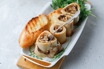 Homemade Roasted Beef Bone Marrow with bread crumbs, spoon and croutons on plate, wooden board grey background. Flat lay.