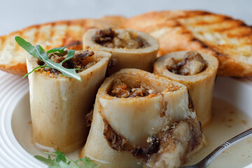 Homemade Roasted Beef Bone Marrow in broth with croutons and spoon on plate grey background. Side View. Close up.