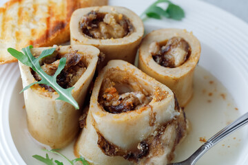 Homemade Roasted Bone Marrow in beef broth with croutons and spoon on plate grey background. Side View. Close up.