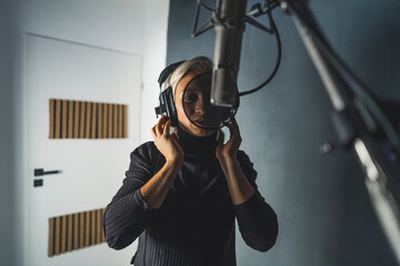 Beautiful blonde girl singing song in recording studio with professional microphone and headphones,...