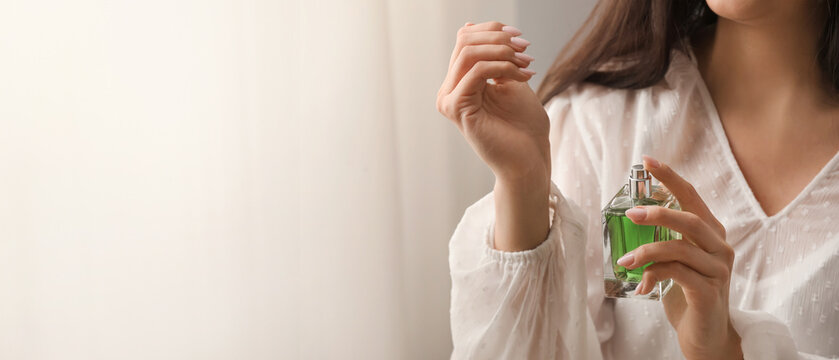 Young woman with bottle of perfume at home, closeup. Banner for design