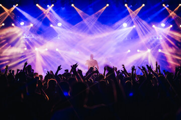 Crowd is rising their hands and dancing on a music festival concert at night.
