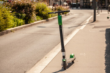 Selective blur on a black and green electric scooter for rent, available in the streets of Lyon, France, standing alone, belonging to a tech company specialized in vehicle sharing.