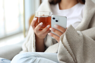 Young woman with cup of tea using mobile phone on her day off at home, closeup