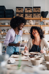 Interracial women having wine and chatting on pottery class in studio.