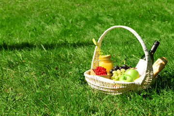 Wicker basket with tasty food and drinks for romantic picnic on grass in park