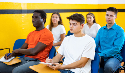 Women and men sitting at desks and listening to lecture in taxi training school.