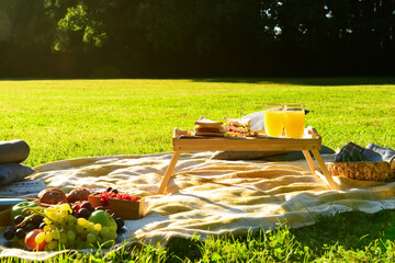Set for romantic picnic with tasty food and glasses of juice on green grass in park