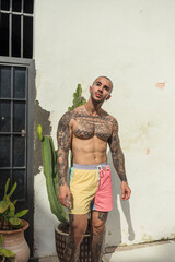 Chico joven tatuado y fitness posando en bañador en piscina de hotel 