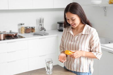 Young Asian woman taking pills from bottle in kitchen