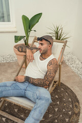 Chico joven tatuado y fitness sentado en silla en piscina de hotel