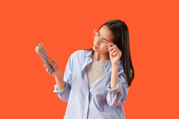 Female designer in eyeglasses with paint color palettes squinting on orange background