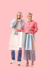 Mature woman with shopping bags and her shocked husband on pink background