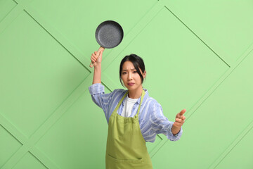 Naklejka premium Portrait of young Asian woman with frying pan on green background