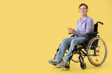 Young man in wheelchair with headphones and mobile phone on yellow background